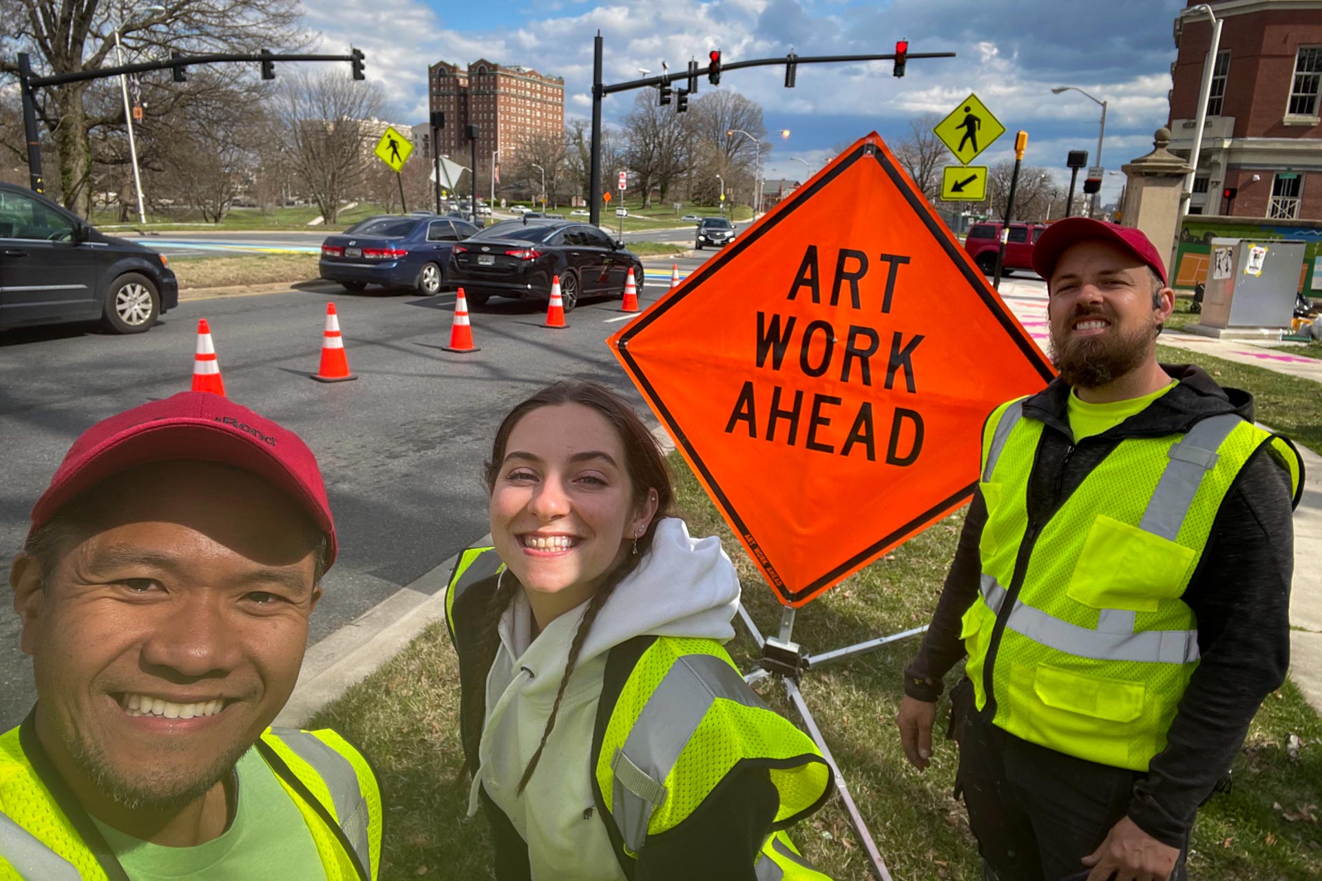 Druid Hill Canopy Crosswalk Graham Projects install team selfie with Kylee, Graham, and Melvin in front of a large ART WORK AHEAD sign